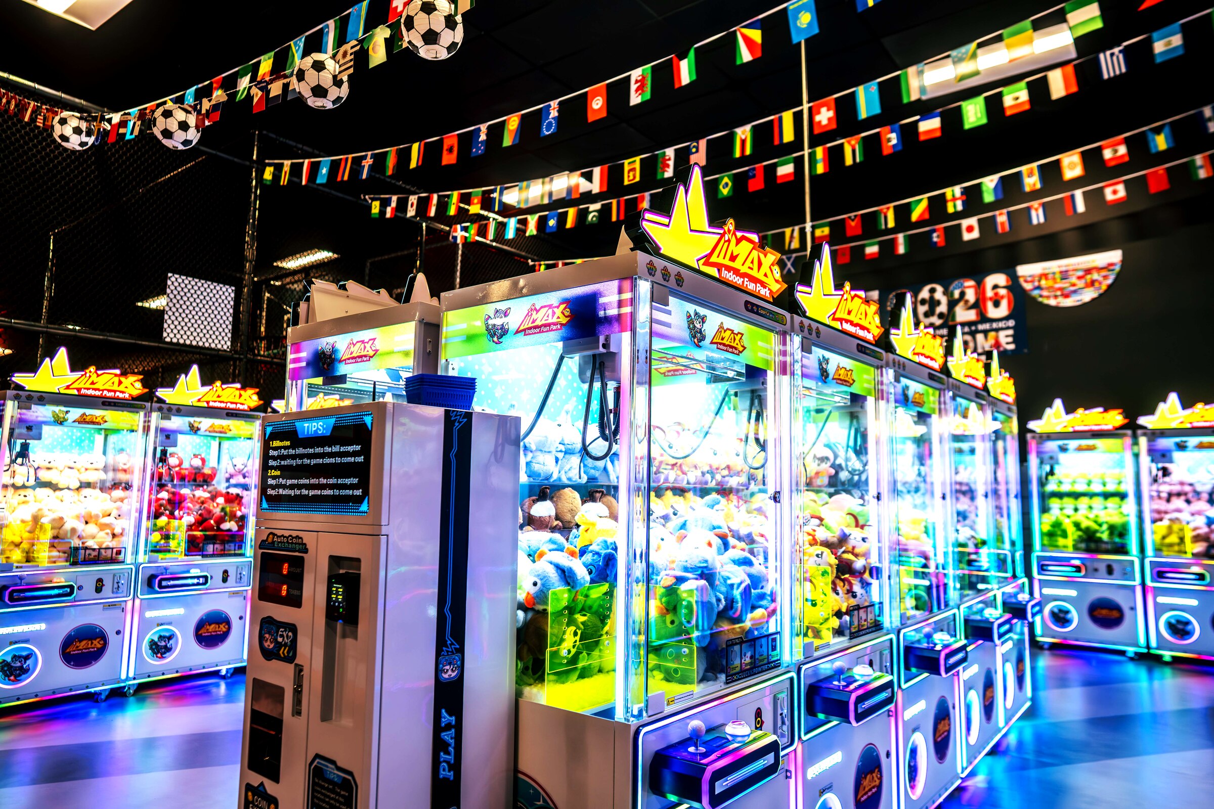 A row of premium commercial claw machines with LED lighting in a modern indoor fun park